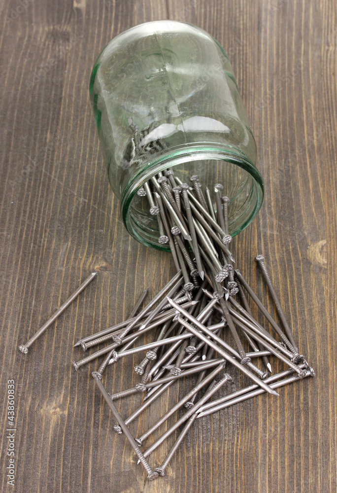 Wall mural Metal nails and glass jar on wooden background