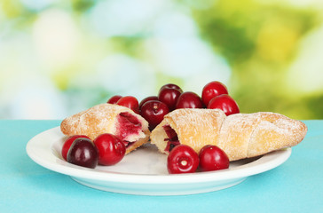 white plate with croissant and cherry on green background