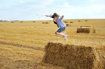 Naklejka na ściany i meble Little girl jumping from a top of haystack