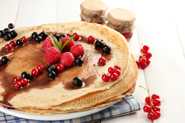Delicious pancakes with berries and jam on plate on wooden