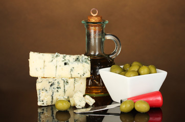 Cheese with mold and olives on brown background close-up