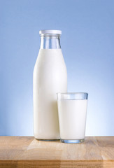 Bottle of fresh milk and glass is wooden table on a blue backgro