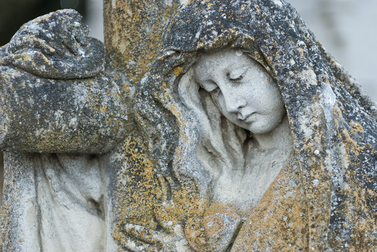 Estatua de una mujer agarrada a una cruz en un cementerio.