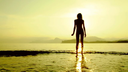 Beautiful woman walking along the coastline at sunset