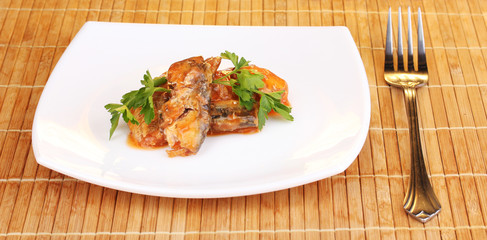 Tasty sardines on plate on wooden mat on brown background