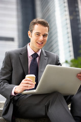 Businessman Working On Laptop Outside Office With Coffee