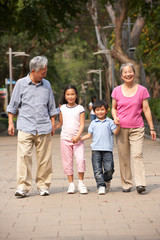 Chinese Grandparents Walking Through Park With Grandchildren