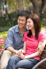 Fototapeta na wymiar Young Chinese Couple Relaxing On Park Bench Together