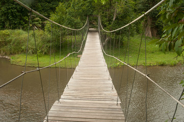 Wood hanging bridge across river in forest.