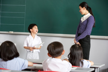 Pupil And Teacher Standing By Blackboard In Chinese Classroom