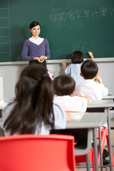 Female Pupil Writing On Blackboard In Chinese Classroom