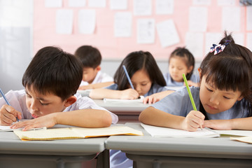 Group Of Students Working At Desks In Chinese School Classroom