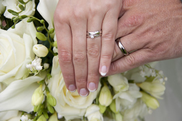 wedding rings on bride and groom against a white wedding bouquet 