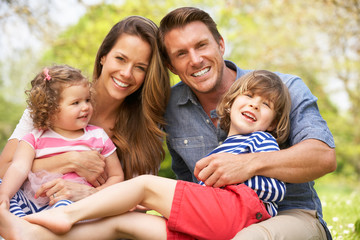 Parents Sitting With Children In Field Of Summer Flowers