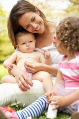 Mother Sitting With Daughters In Field Of Summer Flowers