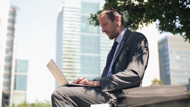 Young handsome businessman working on laptop in the city