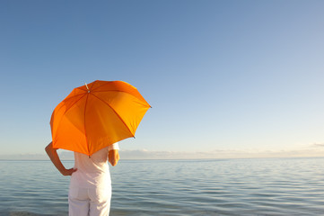 Woman with orange umbrella at ocean background