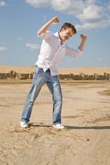 Young man in white shirt and blue jeans standing on the sand