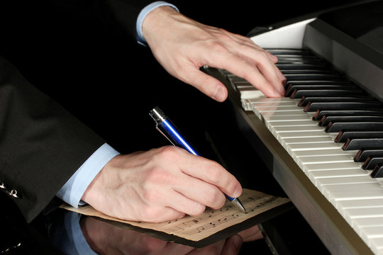 man hands playing piano and writes on parer for notes