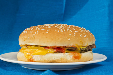 Cheeseburger lying on a white plate with blue linen background