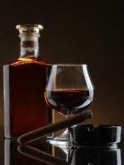 bottle and glass of brandy and cigar on brown background