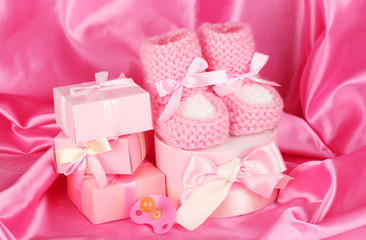 pink baby boots, pacifier, gifts on silk background.