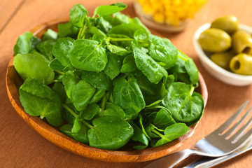 Fresh watercress on wooden plate with olives and corn