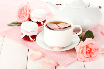 Fototapeta na wymiar teapot and cup of tea with roses and jam on white wooden table