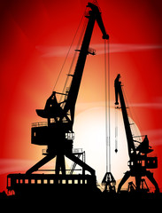 Silhouettes of two port cranes on a sunset