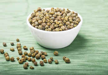 Green pepper. Dried green peppercorns in a white porcelain bowl on green textile made of linen. Macro photo.