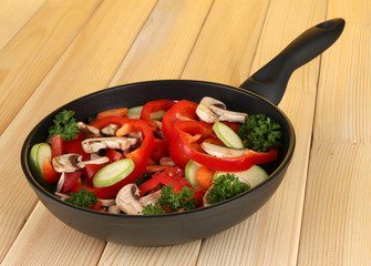 frying pan with vegetables on wooden background