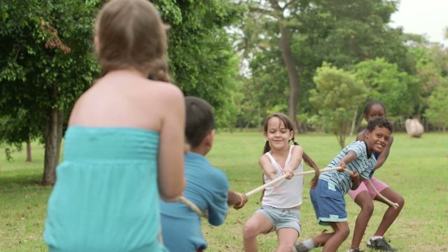Happy school children playing tug of war in park