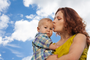 mother kissing her baby on cloudy background