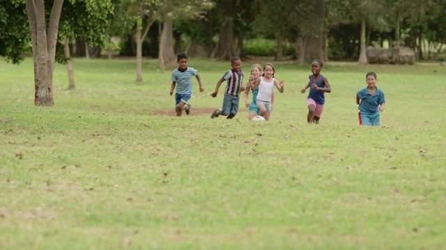 Boys and girls playing football in park. Slow motion