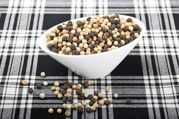 French mignonette pepper corns. White and black peppercorns in a white porcelain bowl on black and...