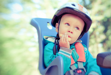Little boy in bike child seat eating cracker. Cross process