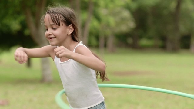 Happy little girl playing hula hoop in park. Slow motion