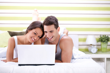 Young couple using laptop while lying on bed