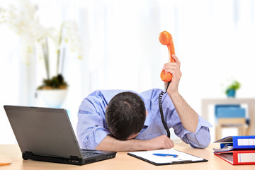 Exhausted businessman holding a telephone in his office