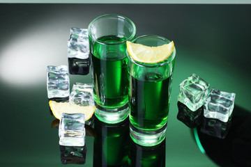 Two glasses of absinthe, lemon and ice on green background