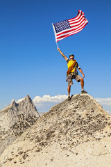 Fototapeta premium Climber waves flag on mountain peak.