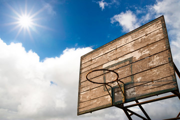Grunge wooden basket hoop against sunrise on cloud blue sky