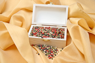 Pepper treasure. Mixed dried peppercorns in a wooden box on cream colored silk.