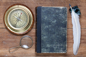 Compass, antique book, magnifying glass, quill, inkwell on wood