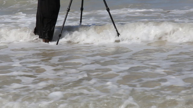 Photographer with tripod in the wave of sea