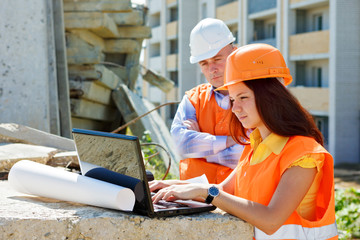 Female architect and construction worker looking at laptop toget