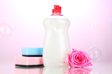 Dishwashing liquid with sponges and flower on pink background