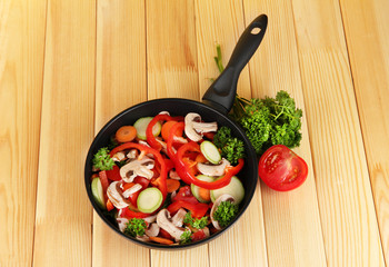 frying pan with vegetables on wooden background