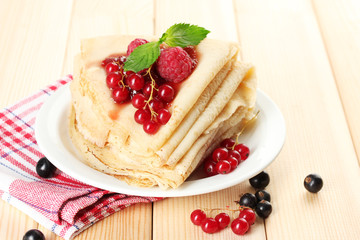 Delicious pancakes with berries and jam on plate on wooden