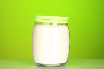 Jar with white crystal sugar on colorful background